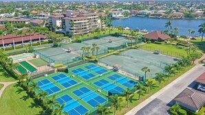 Suuri tenniskeskus, jossa on useita kenttiä, ja jonka ympärillä on vehreää kasvillisuutta ja vesialue.