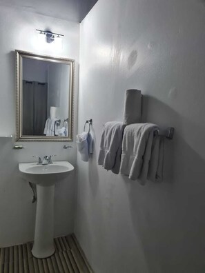A bathroom with a white sink, a mirror, and a towel rack with towels. - Sky Beach Rooms (Montego Bay)
