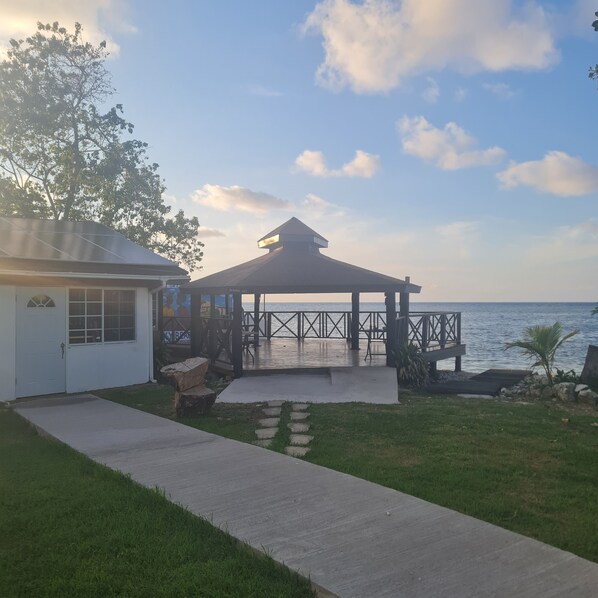 A gazebo with a view of the sea, a pathway leading to a house, and a grassy area. - Sky Beach Rooms (Montego Bay)
