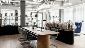 Un espacio de oficina moderno con una mesa de madera larga, sillas negras y plantas en macetas.