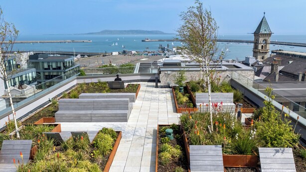 Un jardín en la azotea con jardineras escalonadas y vistas al mar y a una torre del reloj.