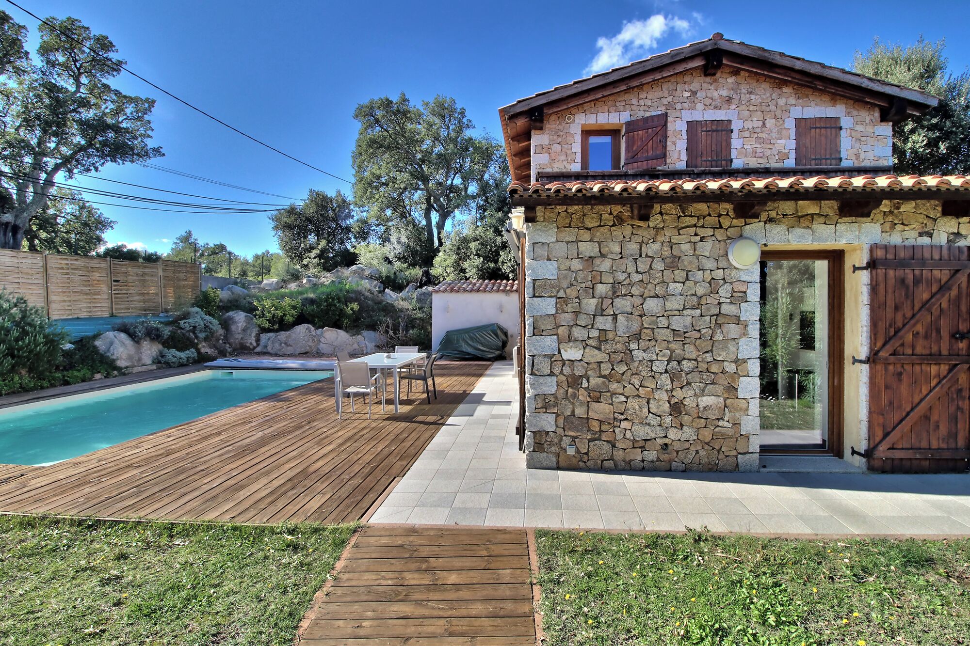 A stone house with a wooden deck and a swimming pool.