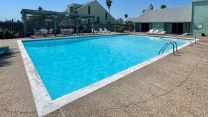 A rectangular swimming pool with a white border, surrounded by lounge chairs and a covered seating area. - Coastal Cozy and a View by Silver Sands Vacation Rentals (Corpus Christi)