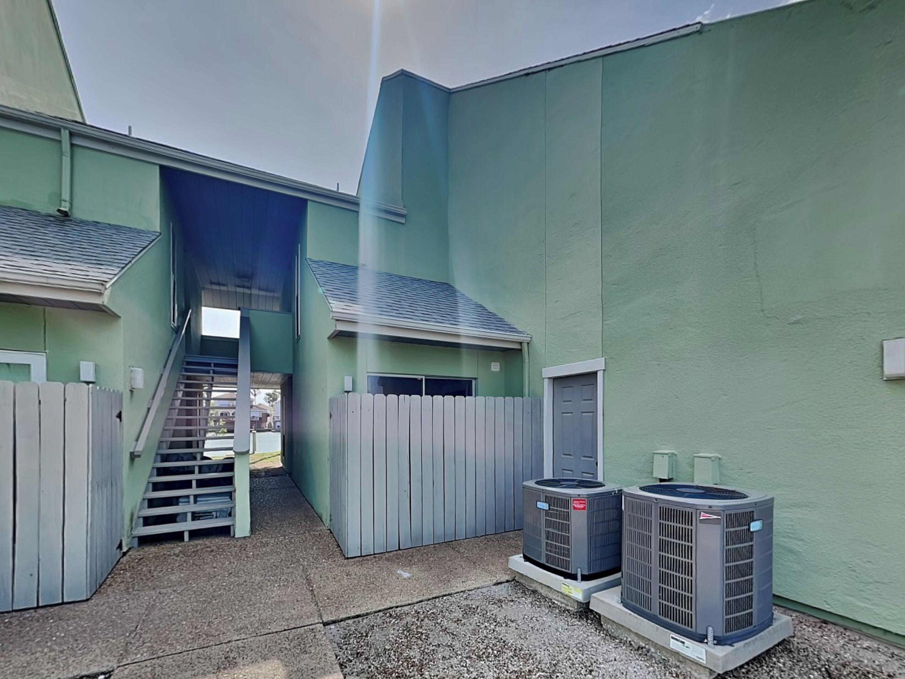 Een gebouw met een trap die naar een hoger gelegen deel leidt, een omheind gebied en twee airconditioners.