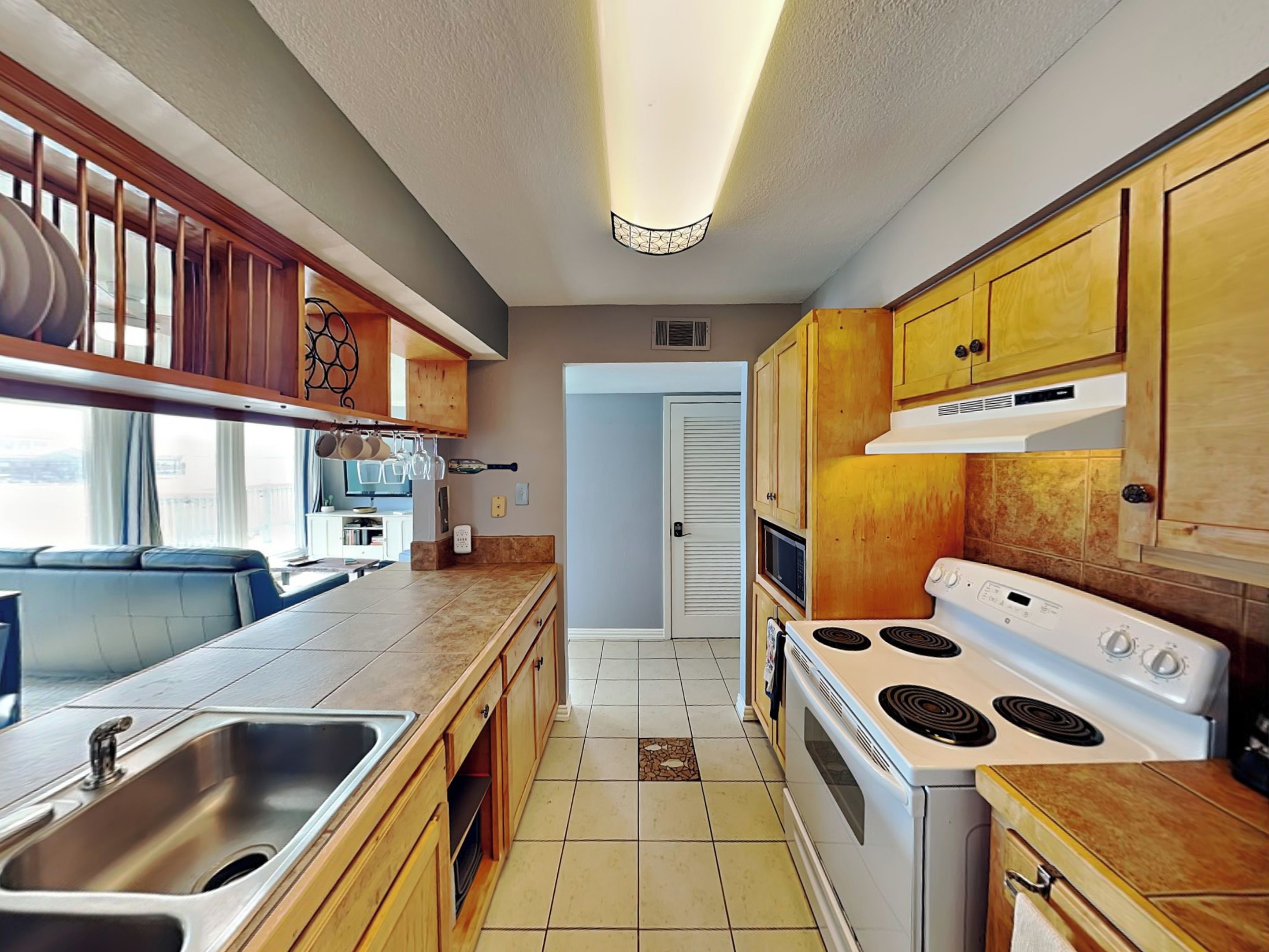 Een kleine keuken met houten kastjes, een witte kookplaat en een roestvrijstalen spoelbak.