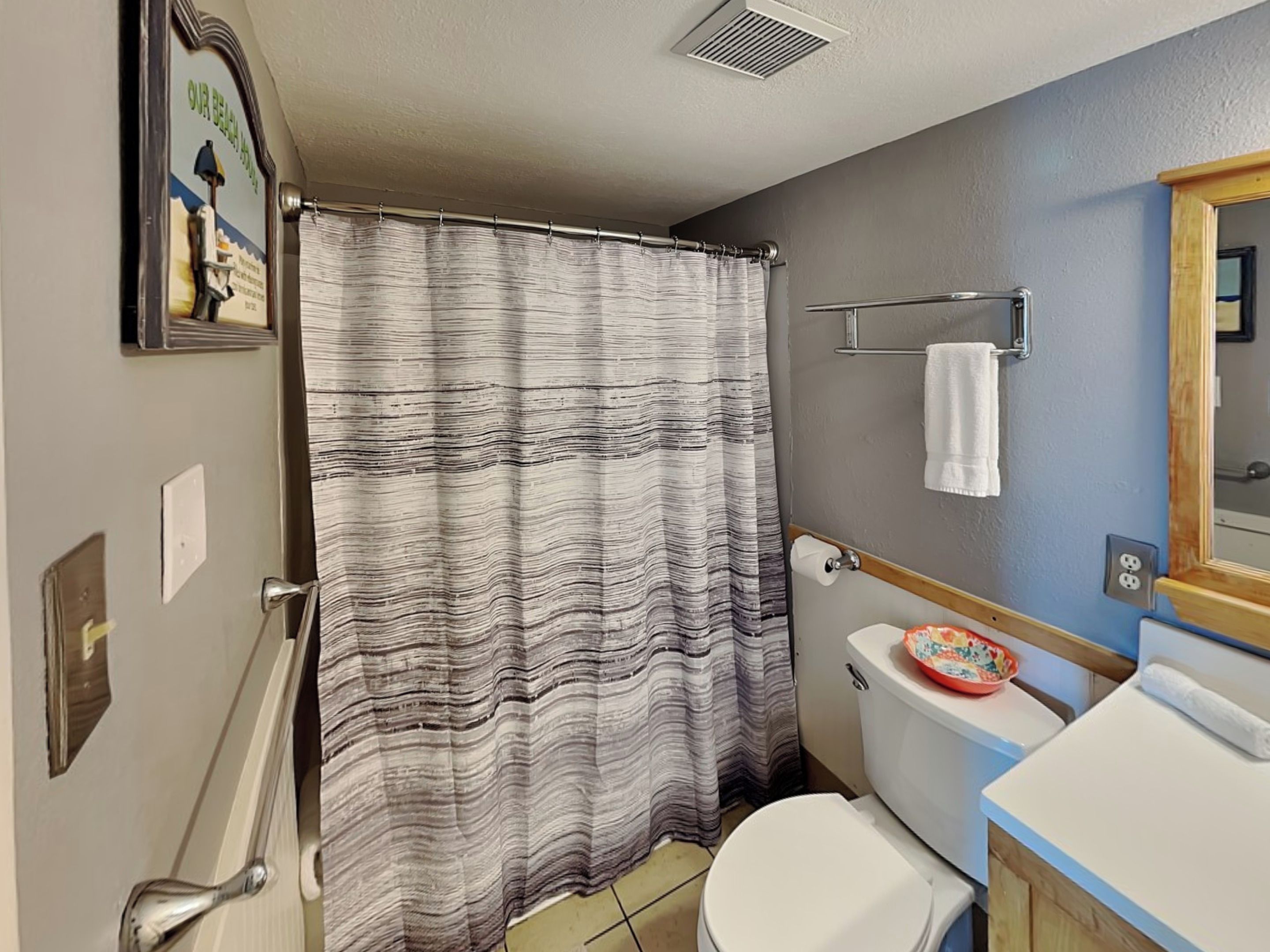A bathroom with a striped shower curtain, a toilet, a sink with a decorative bowl, and a mirror.