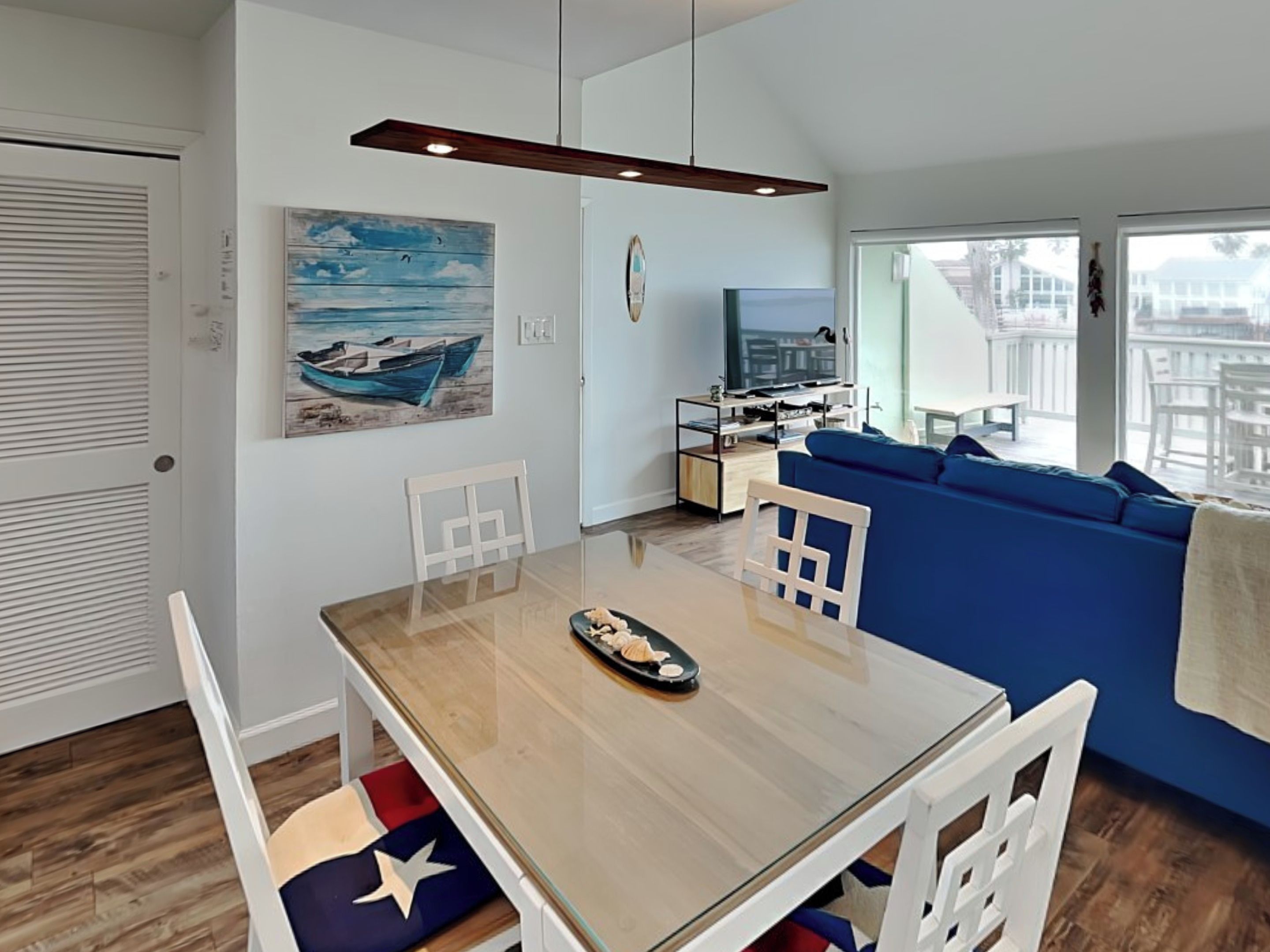 Un salon moderne avec un canapé bleu, une table à manger en bois avec des chaises, un téléviseur et un tableau représentant un bateau accroché au mur.