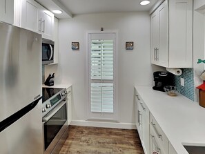 A modern kitchen with white cabinets, stainless steel appliances, and a wooden floor. - Sunset Water View by Silver Sands Vacation Rentals (Corpus Christi)