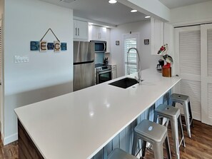 Une cuisine moderne avec des meubles blancs, des appareils en acier inoxydable et un îlot central doté de tabourets de bar.