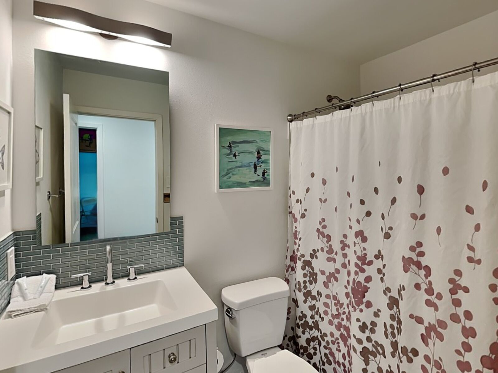 Une salle de bain avec un lavabo blanc, des toilettes et un rideau de douche orné d’un motif de feuilles.