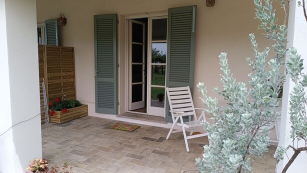 A covered patio area with a wooden bench, a potted plant, and a sliding glass door. - Pepe Apartment: Peace and Relaxation in the Maremma countryside. (Toscana)