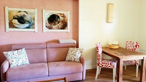 A living room with a sofa, two patterned cushions, a wooden table with two chairs, and two wall-mounted artworks. - Pepe Apartment: Peace and Relaxation in the Maremma countryside. (Toscana)