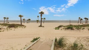 A beach with a wooden pathway leading to the water, surrounded by palm trees and clear skies.