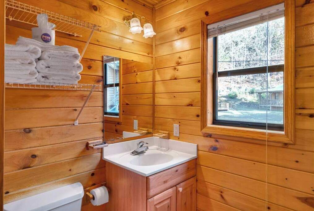 Une salle de bain rustique, avec des murs en bois, comprenant un lavabo, un miroir et un porte-serviettes.