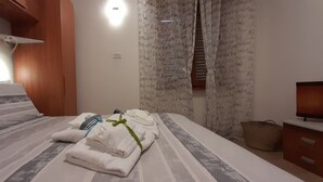 Habitación de hotel con cama, almohadas, mesita de noche con lámpara, televisor y cortina con texto.