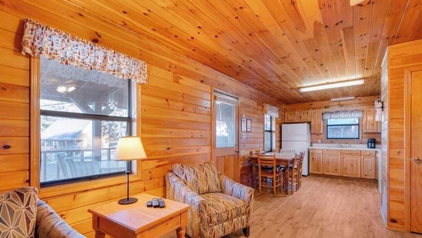 A cozy cabin interior with wooden walls, a dining area, and a kitchen. - Delightful Lakeside 2-Bedroom Cabin on Beautiful Dale Hollow Lake #7! (Byrdstown)