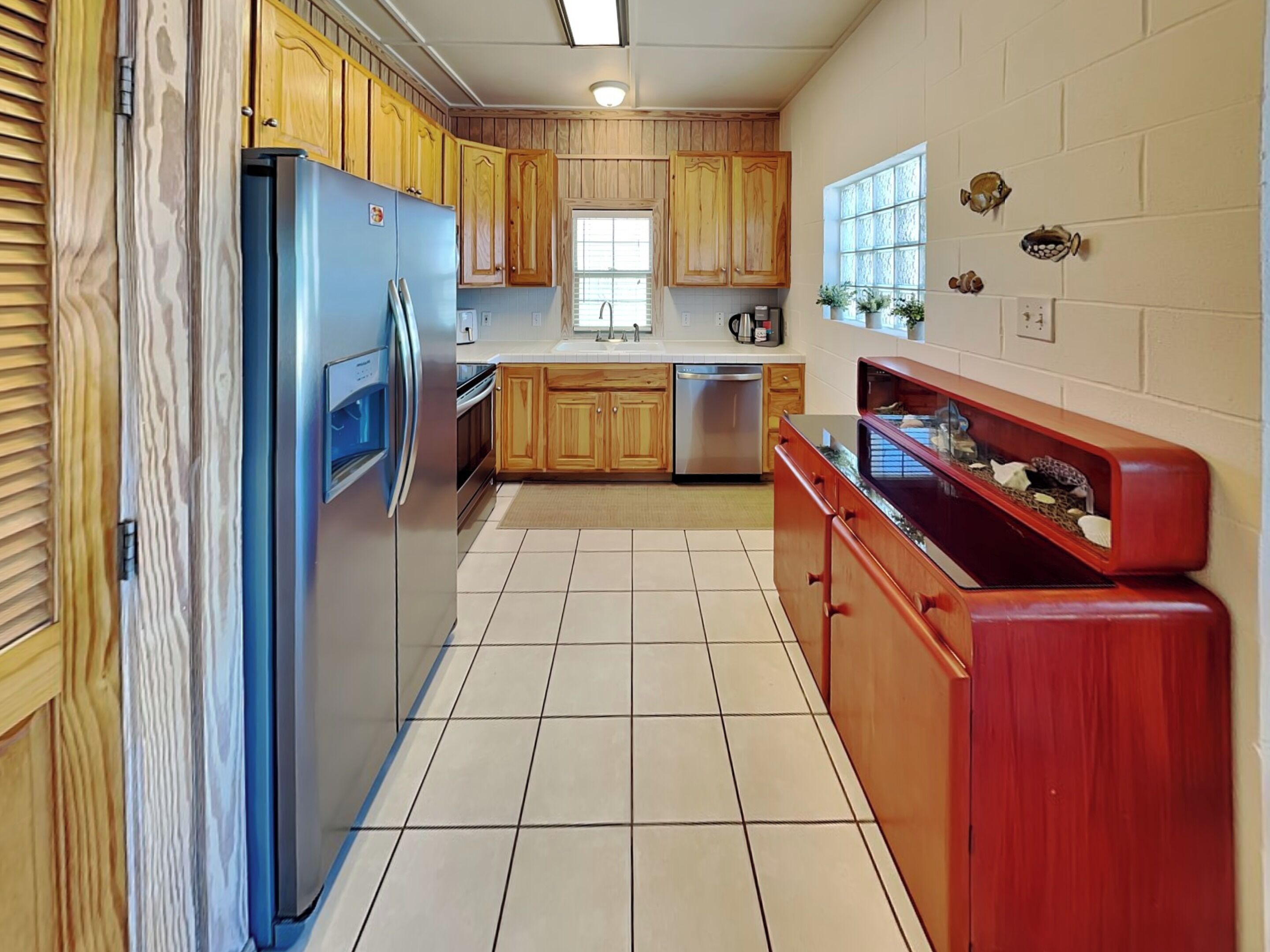 A kitchen with wooden cabinets, a stainless steel refrigerator, a dishwasher, and a red wooden cabinet with decorative items.