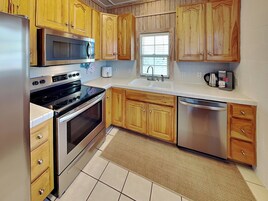 A kitchen with wooden cabinets, stainless steel appliances, a window, and a tiled floor.