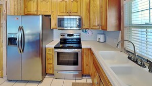 A kitchen with wooden cabinets, a stainless steel refrigerator, an oven, a microwave, and a sink.
