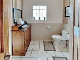 A bathroom with a wooden vanity, a toilet, a window, and a small potted plant.