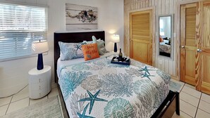 A bedroom with a bed, two bedside lamps, a nightstand, a wooden wardrobe, and a wall-mounted artwork.