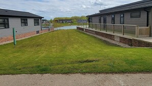 Un edificio moderno con techo plano y ventanas amplias, junto a una zona verde con un sendero que lleva a una masa de agua.