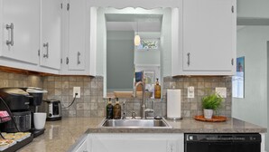 A modern kitchen with white cabinets, a granite countertop, a built-in dishwasher, and a coffee maker. - 2 Homes Together|Sleeps 16|Walk 2 Beach|Firepit (Cocoa Beach)