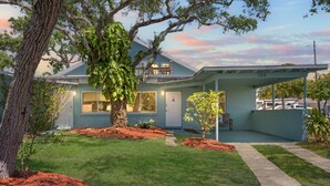 A two-story house with a covered porch, a well-maintained lawn, and a tree in the front yard. - 2 Homes Together|Sleeps 16|Walk 2 Beach|Firepit (Cocoa Beach)