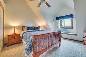 Een slaapkamer met een schuine kap, een houten bed, een nachtkastje, een raam met uitzicht en een plafondventilator.