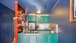 Una cucina con mobili color petrolio, un frigorifero in acciaio inossidabile e un pavimento in legno.