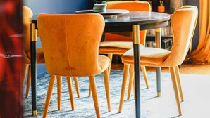 Zona pranzo con tavolo rotondo, sedie arancioni e quadri appesi alle pareti.