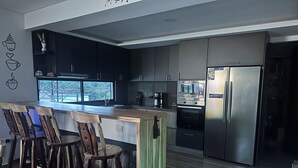 Een moderne keuken met donkere kastjes, een roestvrijstalen koelkast en een barruimte met houten krukken.