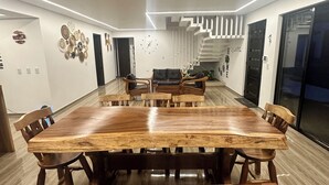 Een moderne eetruimte met een grote houten tafel en banken, een trap en een wandklok.