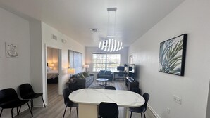 Un salon moderne avec une table à manger en marbre, des chaises noires, un canapé et un téléviseur.