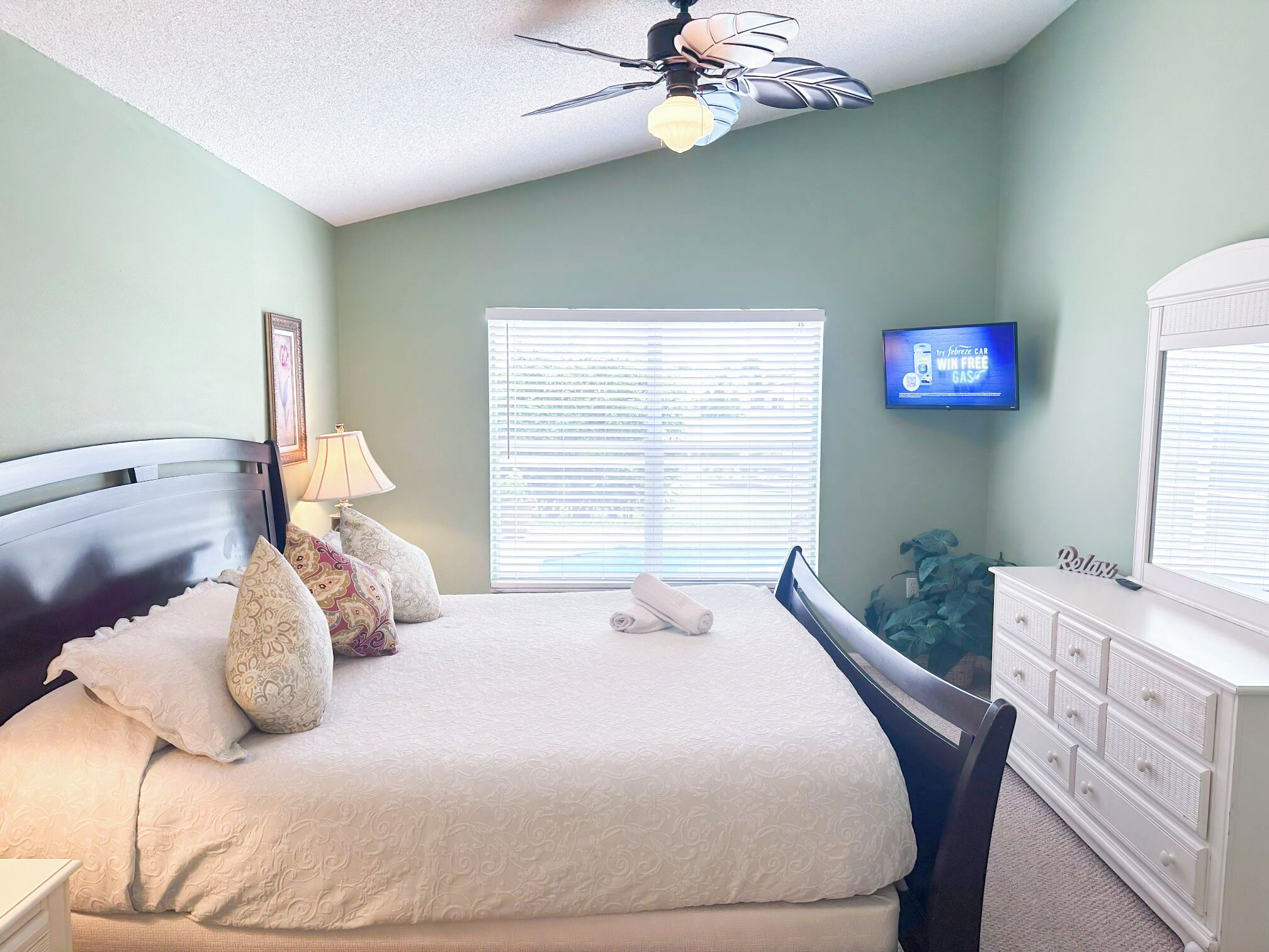 A bedroom with a bed, a nightstand, a lamp, a dresser, a television, and a ceiling fan.