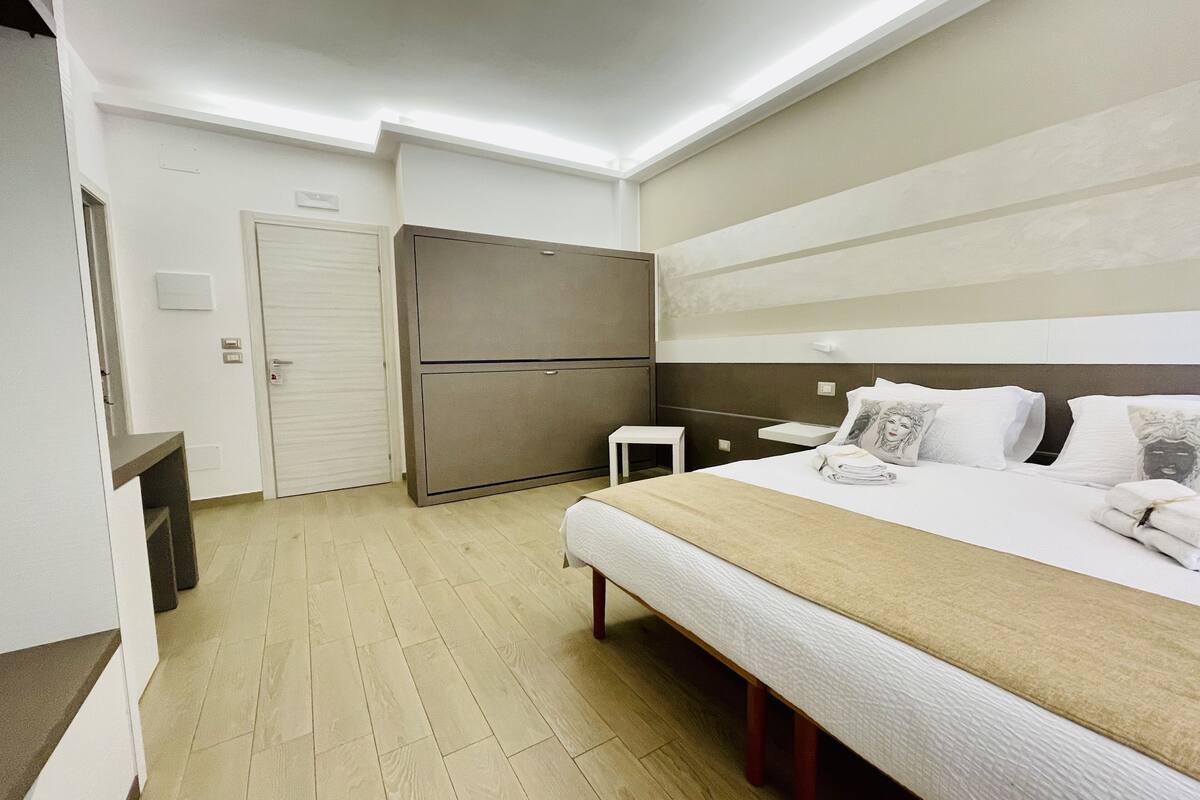 A hotel room with a bed, bedside table, and a wardrobe.