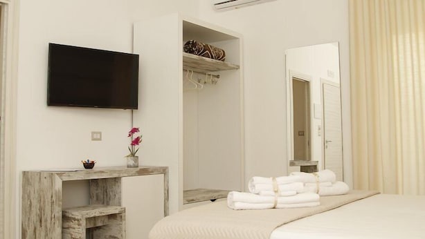 A hotel room with a bed, a TV mounted on the wall, a wooden console table, a mirror, and a bathroom door. - La trinacria (Syracuse)