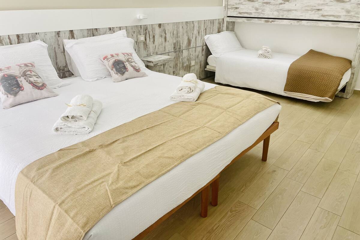 A hotel room with a large bed, a bench, and a massage table.