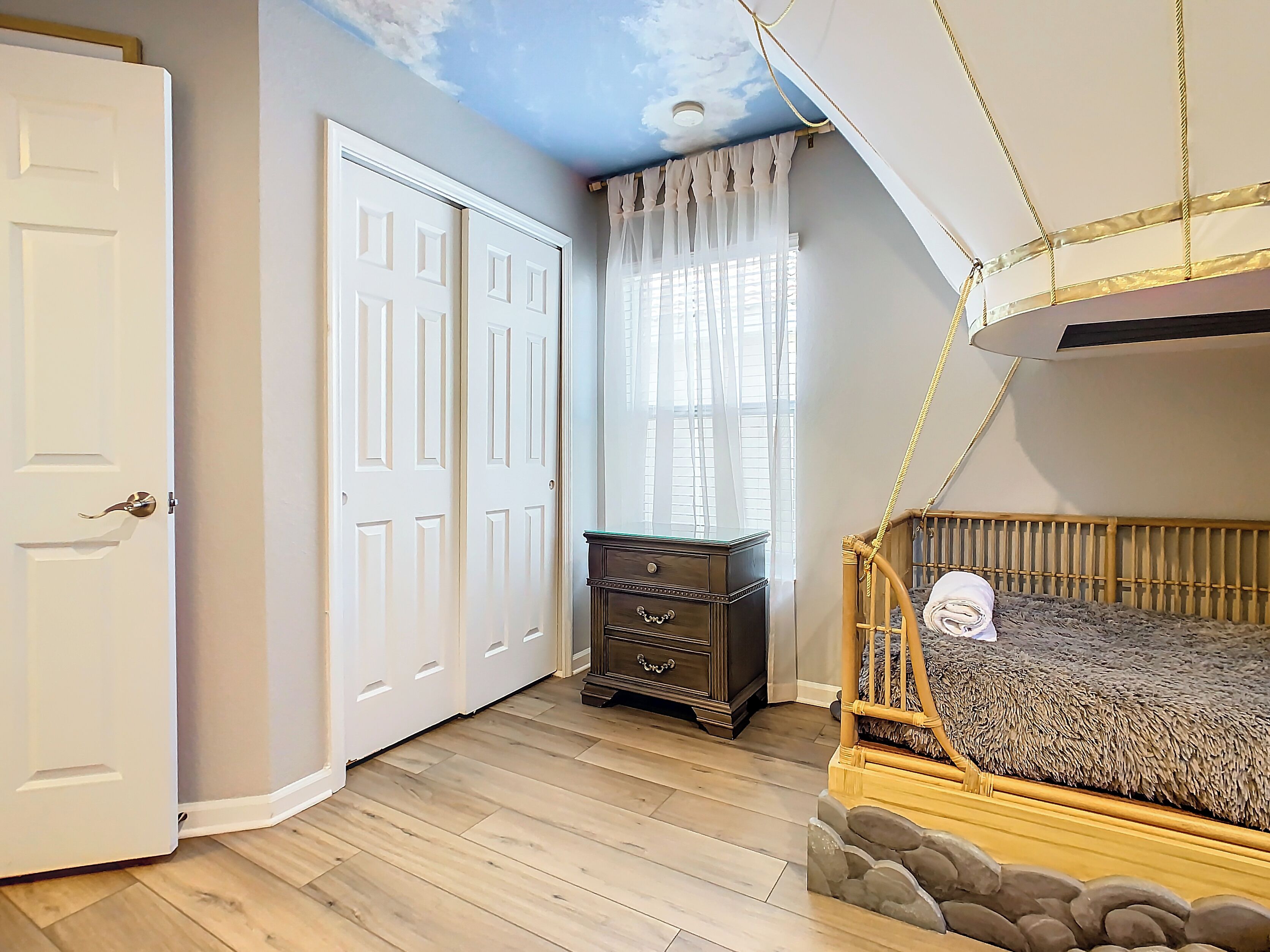 Une chambre avec un lit superposé, une commode, une armoire et un plafond décoré d’un ciel peint.