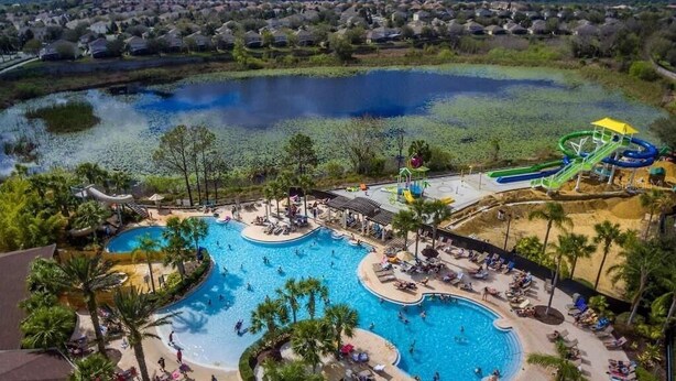 A large outdoor swimming pool with multiple lanes and a water slide, surrounded by palm trees and lounge chairs. - WH7820BS - 5 bedrooms - 5 baths - Nemo and Star Wars  - Big Pool - Theater Room (Kissimmee)