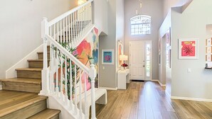 A spacious hallway with wooden flooring, a white staircase with a colorful mural, and a door leading to another room. - WH7820BS - 5 bedrooms - 5 baths - Nemo and Star Wars  - Big Pool - Theater Room (Kissimmee)