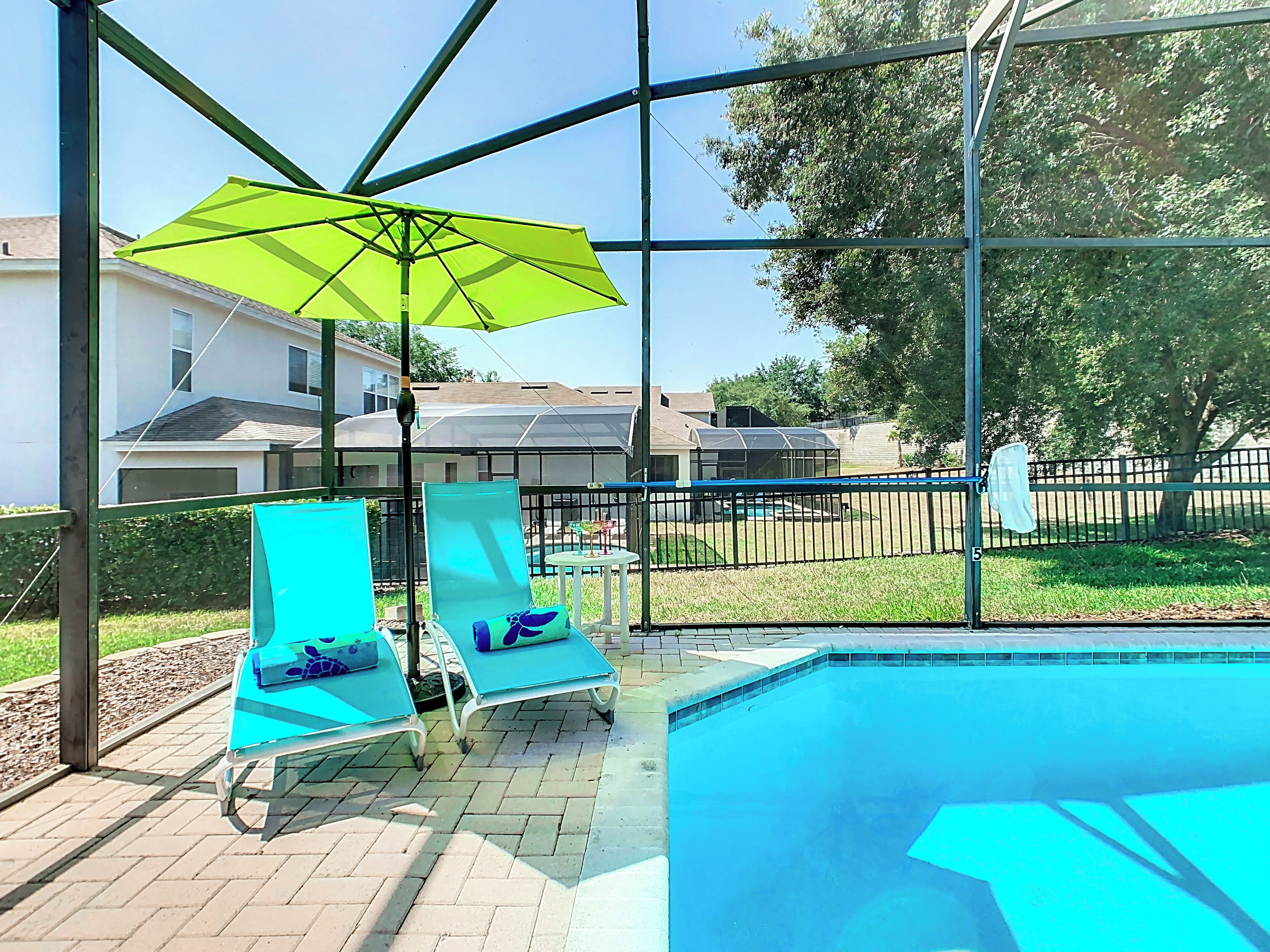 Un área de piscina con dos sillas reclinables azules y una sombrilla verde.