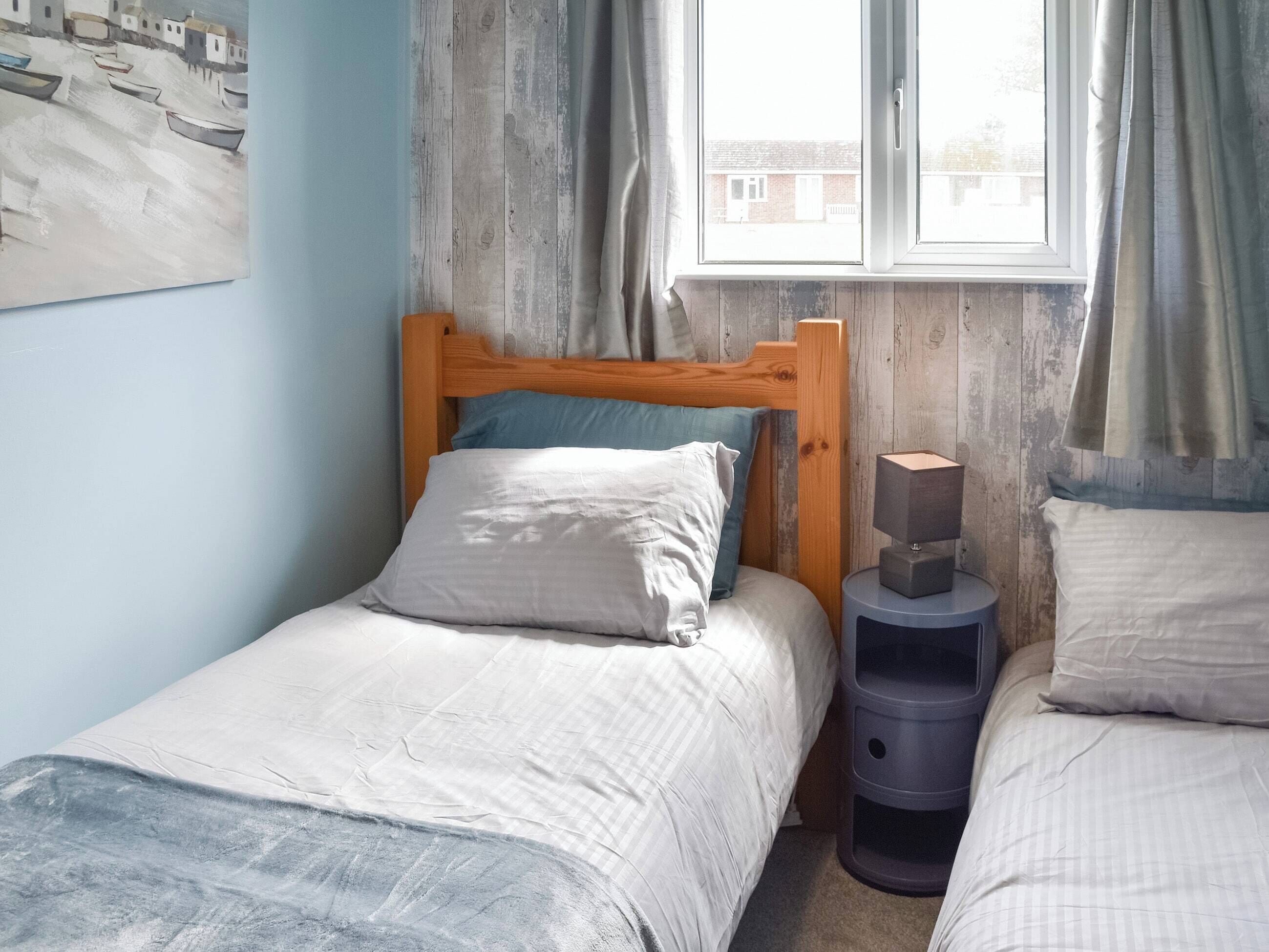 A bedroom with a wooden bed, a bedside table, and a window with curtains.