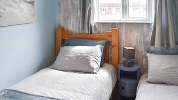 A bedroom with a wooden bed, a bedside table, and a window with curtains.
