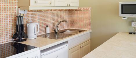 A compact kitchen with a stove, sink, and white cabinets.
