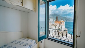 Een slaapkamer met een bed en een raam met uitzicht op een kustplaats en bergen.