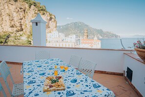 Una terraza con mesa lista para comer, con vistas a un pueblo costero, edificios y acantilados.