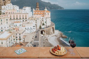 Un paisaje urbano costero con edificios, una playa y una mesa con comida y copas de vino.