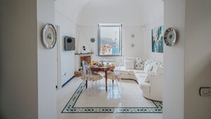 Een moderne woonkamer met een witte bank, een eettafel met stoelen, een open haard en uitzicht op de zee door een groot raam.