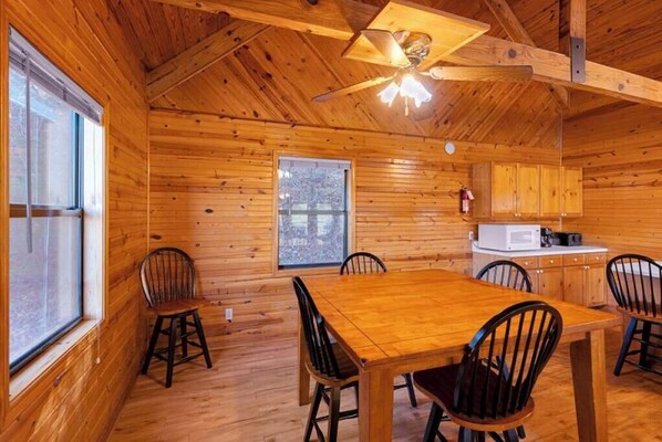 L’intérieur d’une cabane en bois comprend une table à manger, des chaises, un ventilateur de plafond et un coin cuisine.